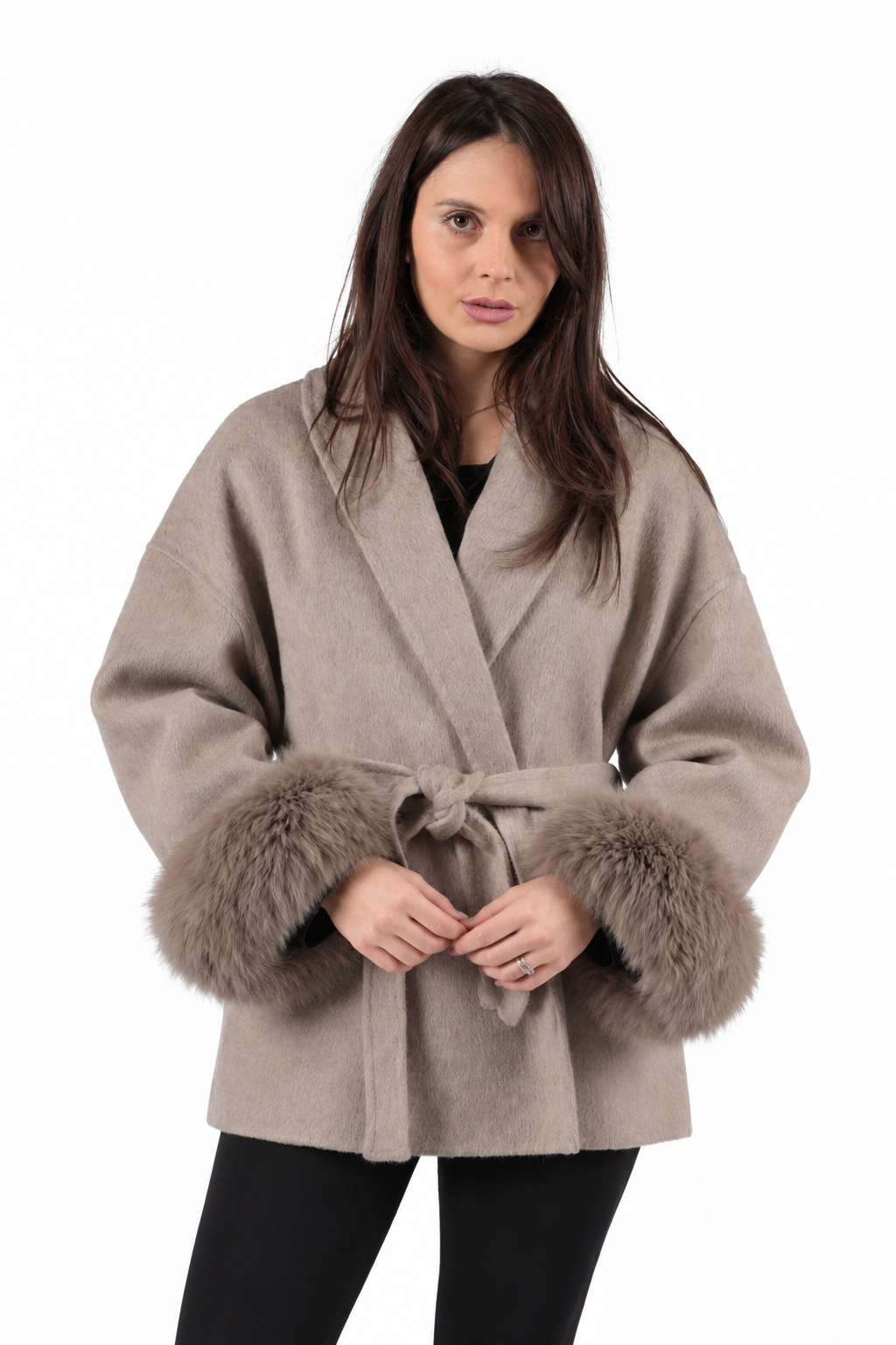 A woman wearing a beige cashmere and wool oat with fox fur cuffs, with black leggings.