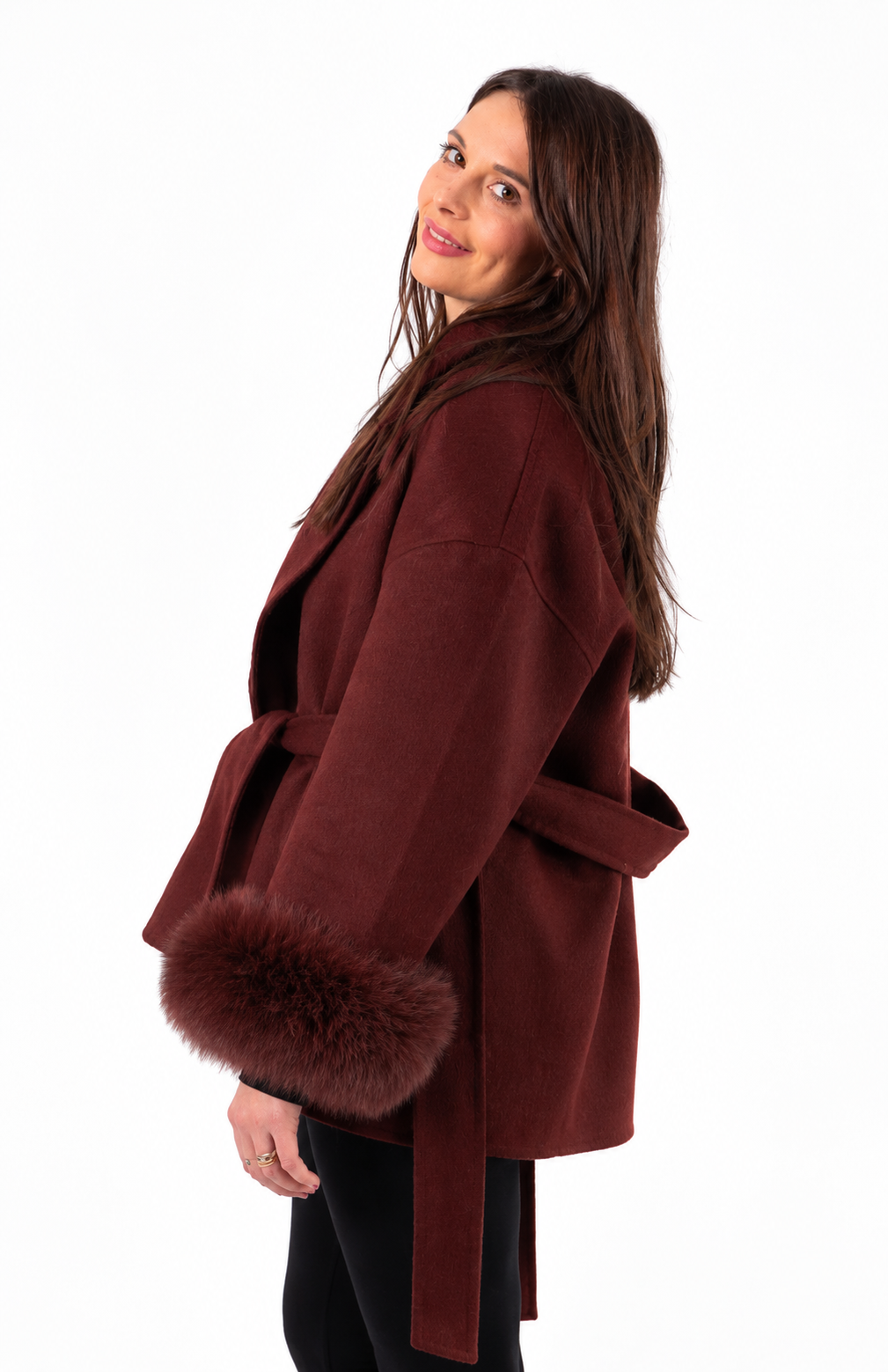 A woman wearing a dark burgundy wrap coat with a matching belt and fluffy fox-fur trimmed detachable cuffs, shown from the side against a plain white background.