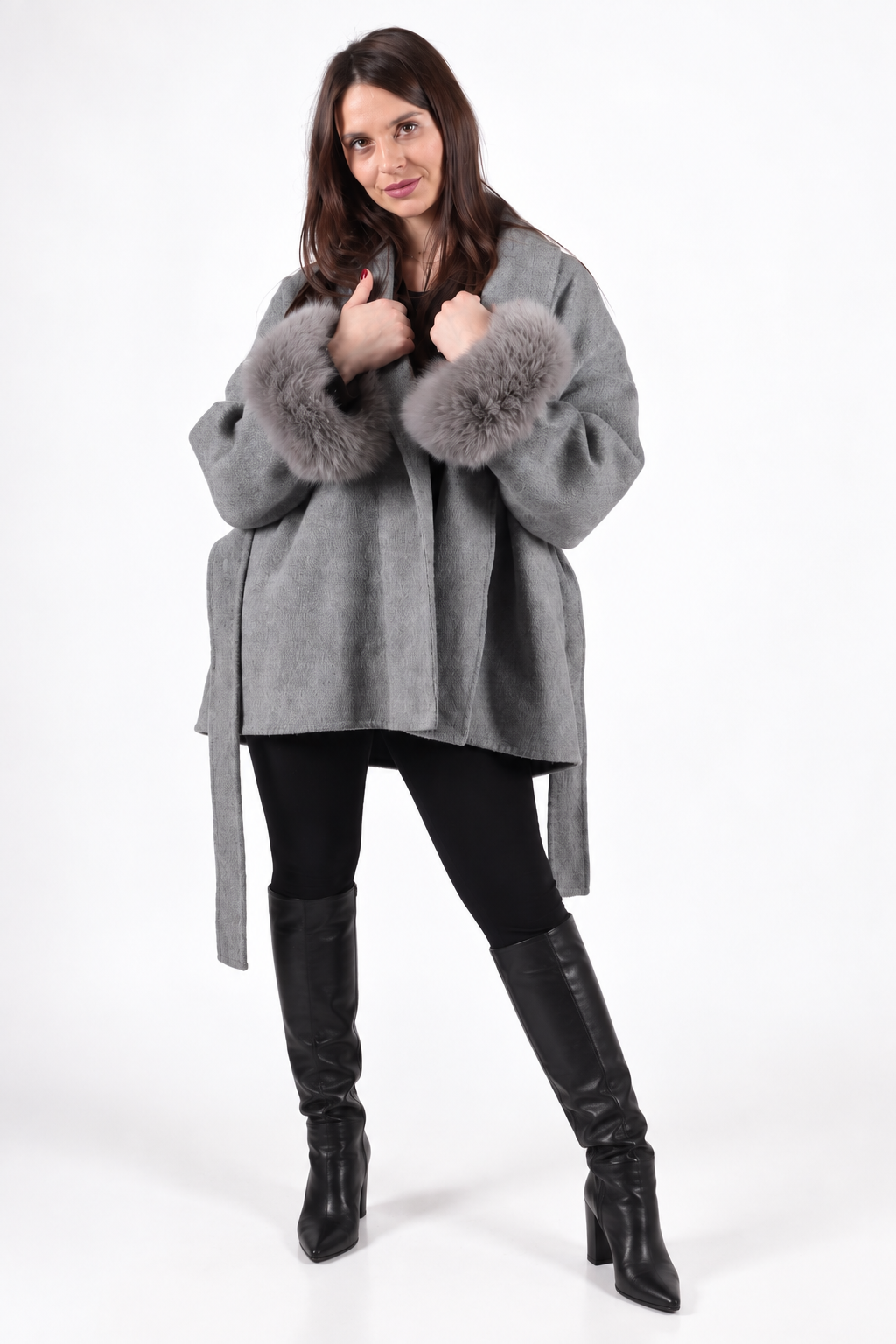 A woman wearing a cashmere and wool grey coat with detachable fox fur a black leggings and black high-knee boots.